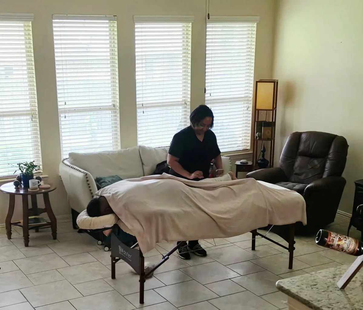 A living room set up for a massage session, table made up beside the windows